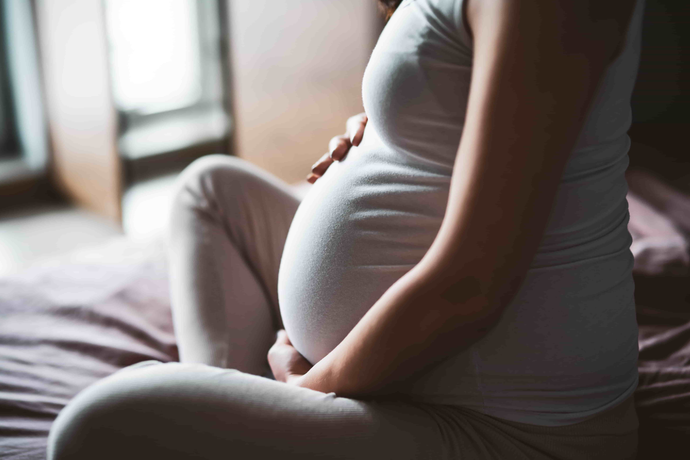 A pregnant woman sitting on a bed. Concept of pregnancy and hair loss.